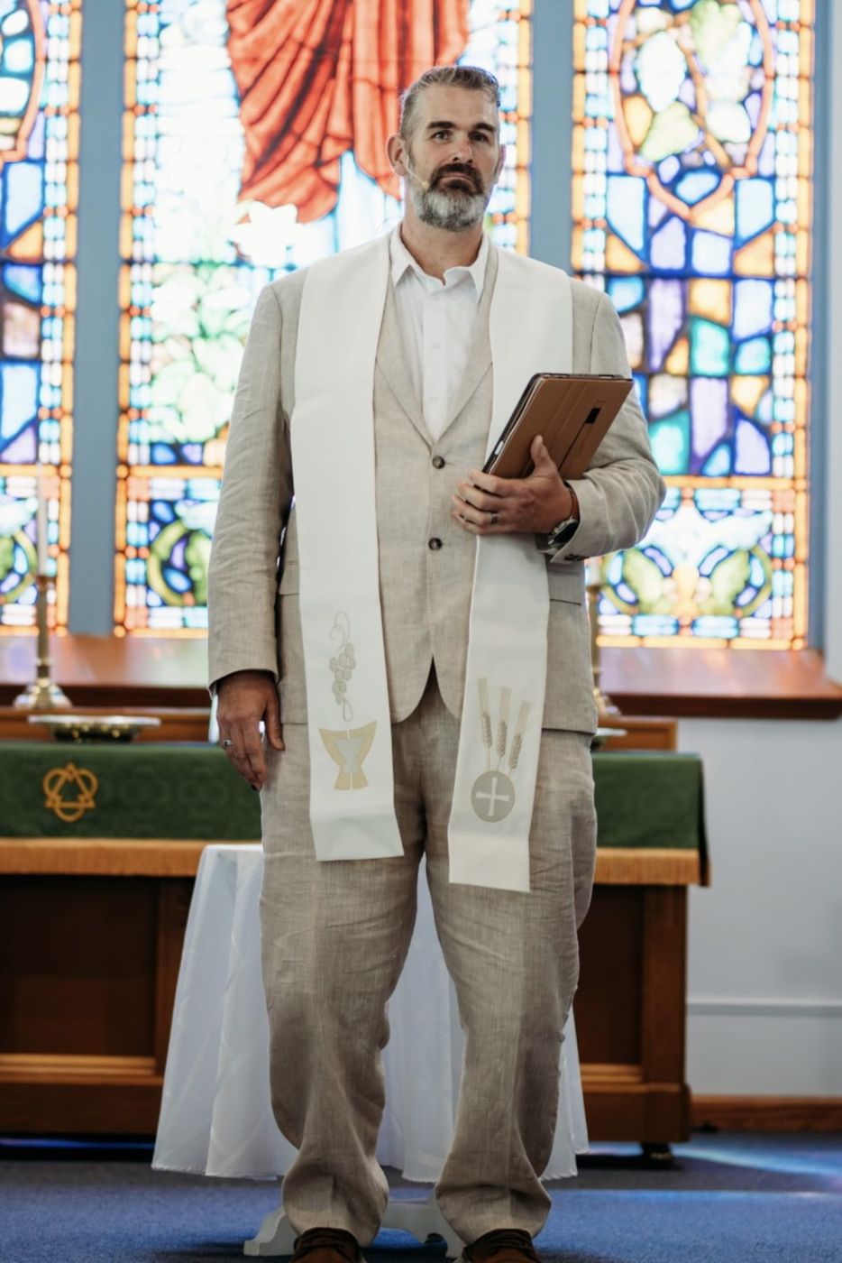 Randy Bennett holding his ceremony notes in a linen suit and white stole